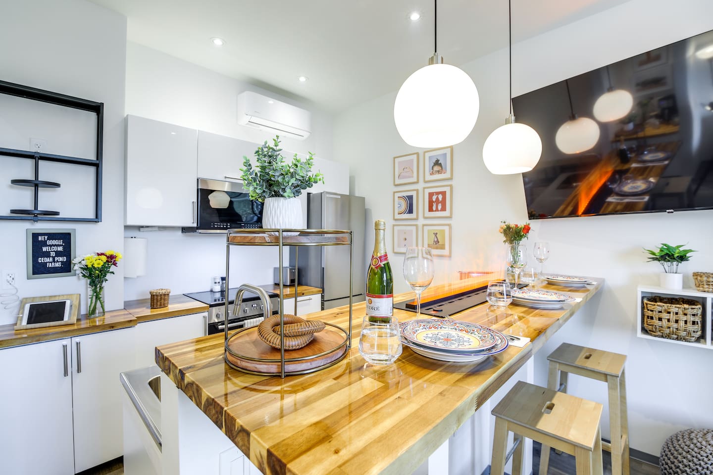 Two stools at the butcher-block breakfast bar of a barndo suite at Cedar Pond Farms, with plates set, fresh flowers out and a welcome board on the counter for arriving guests.